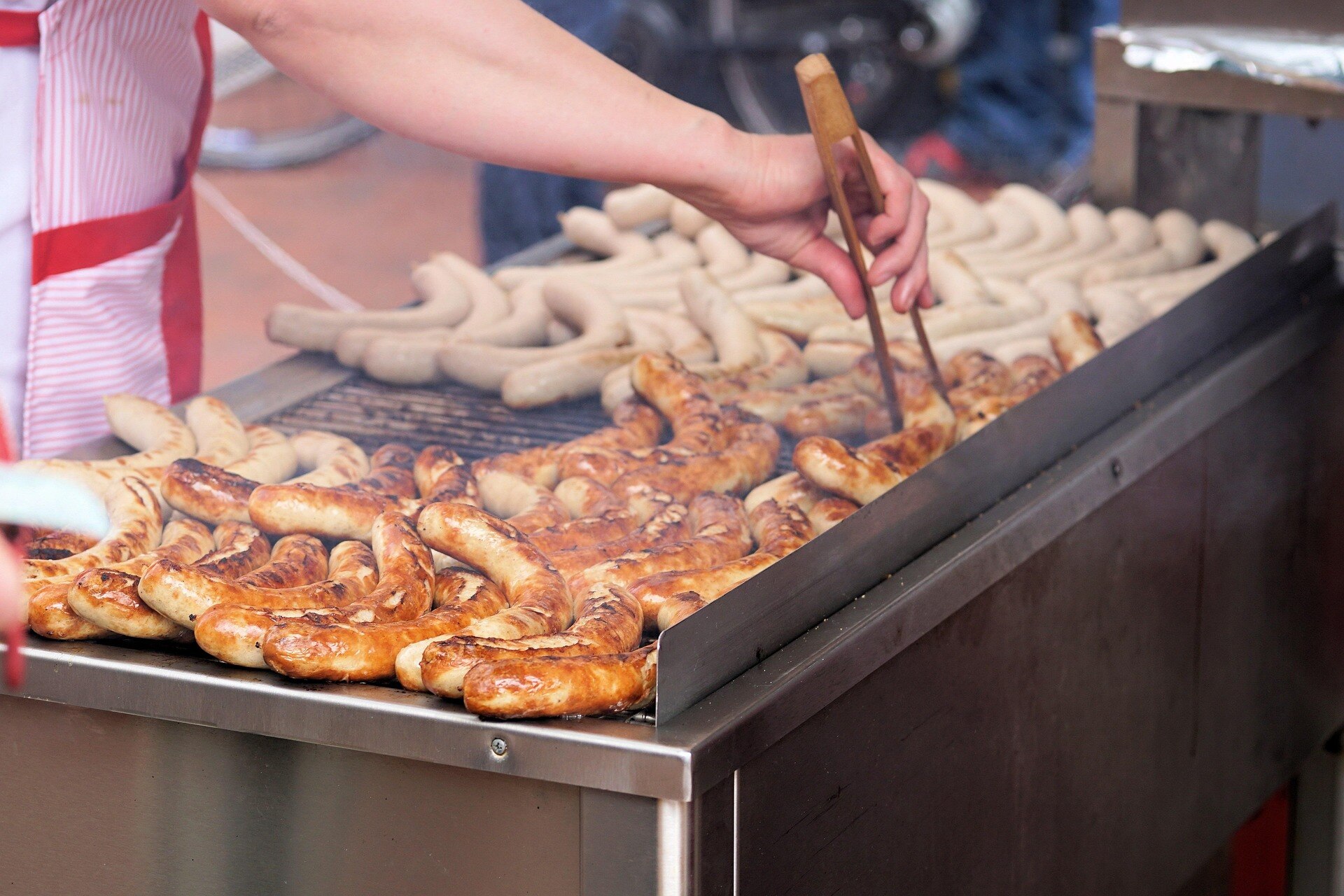 A person stands at a grill, turning sausages.