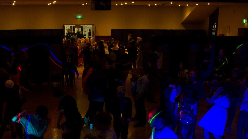 Children dance in a large hall lit with disco lights.