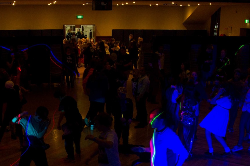 Children dance in a large hall lit with disco lights.