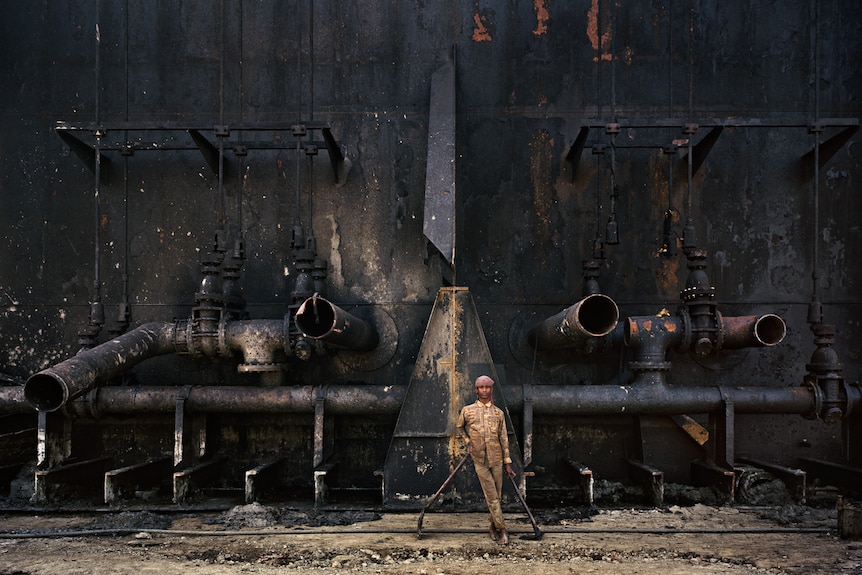 A man in a workers outfit standing next to the side of a ship with open pipes