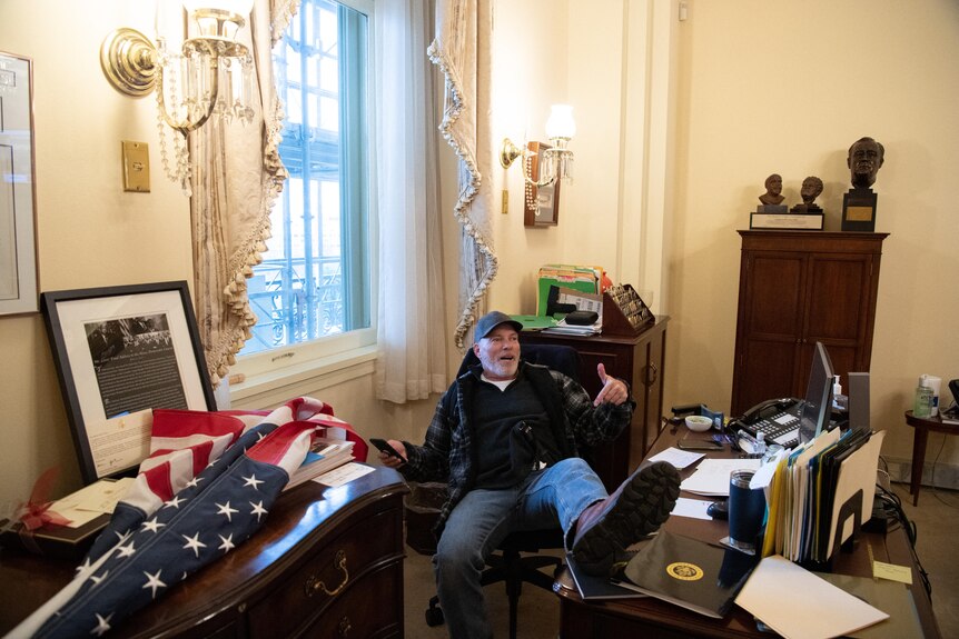 Richard Barnett sits at the desk of Nancy Pelosi during the Capitol riot.
