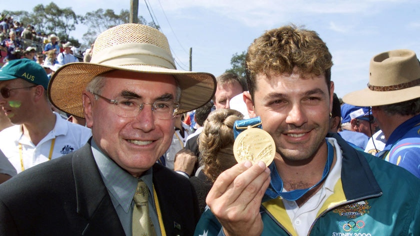Two men smile at the camera, one holding a gold medal.
