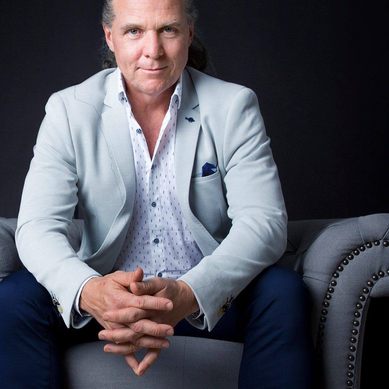 A man with long hair tied back, and wearing a suit.