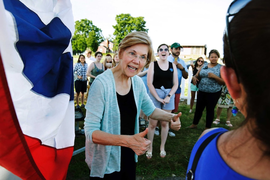 Elizabeth Warren is talking to a voter outside a small town event, with several people looking on behind her