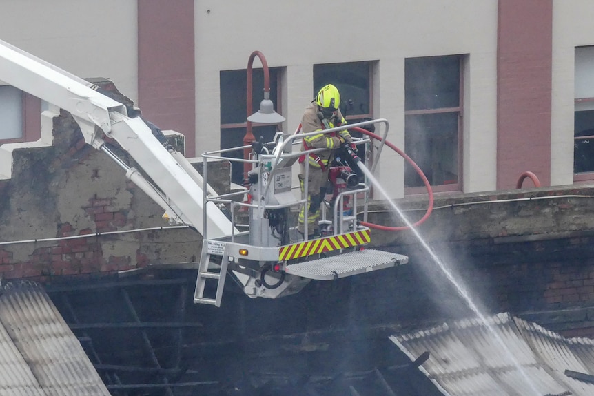 A firefighter on a cherry picker uses a hose to damp down a building. No flames are visible