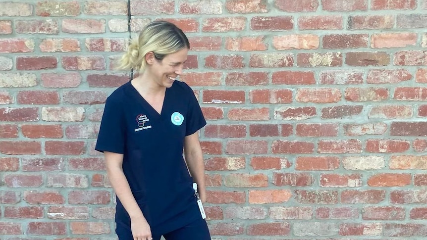 blonde woman in blue nurse scrubs smiling