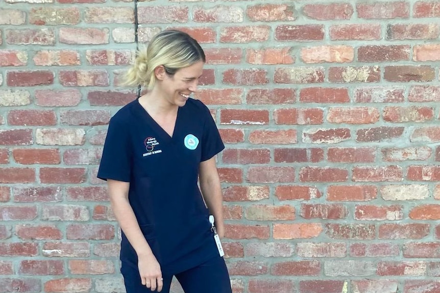 blonde woman in blue nurse scrubs smiling