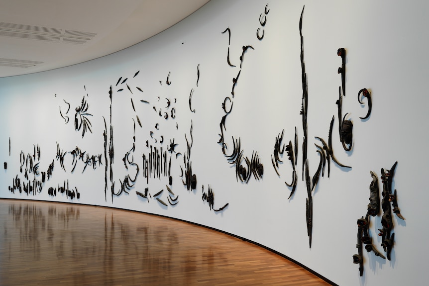 A collection of clay sculptures of burnt banksia forms are affixed to a curved white gallery wall