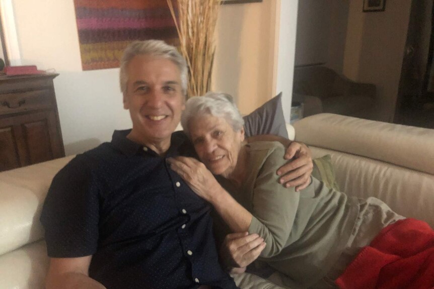 David Desira our his arm around his mother Josephine sitting on a beige couch.