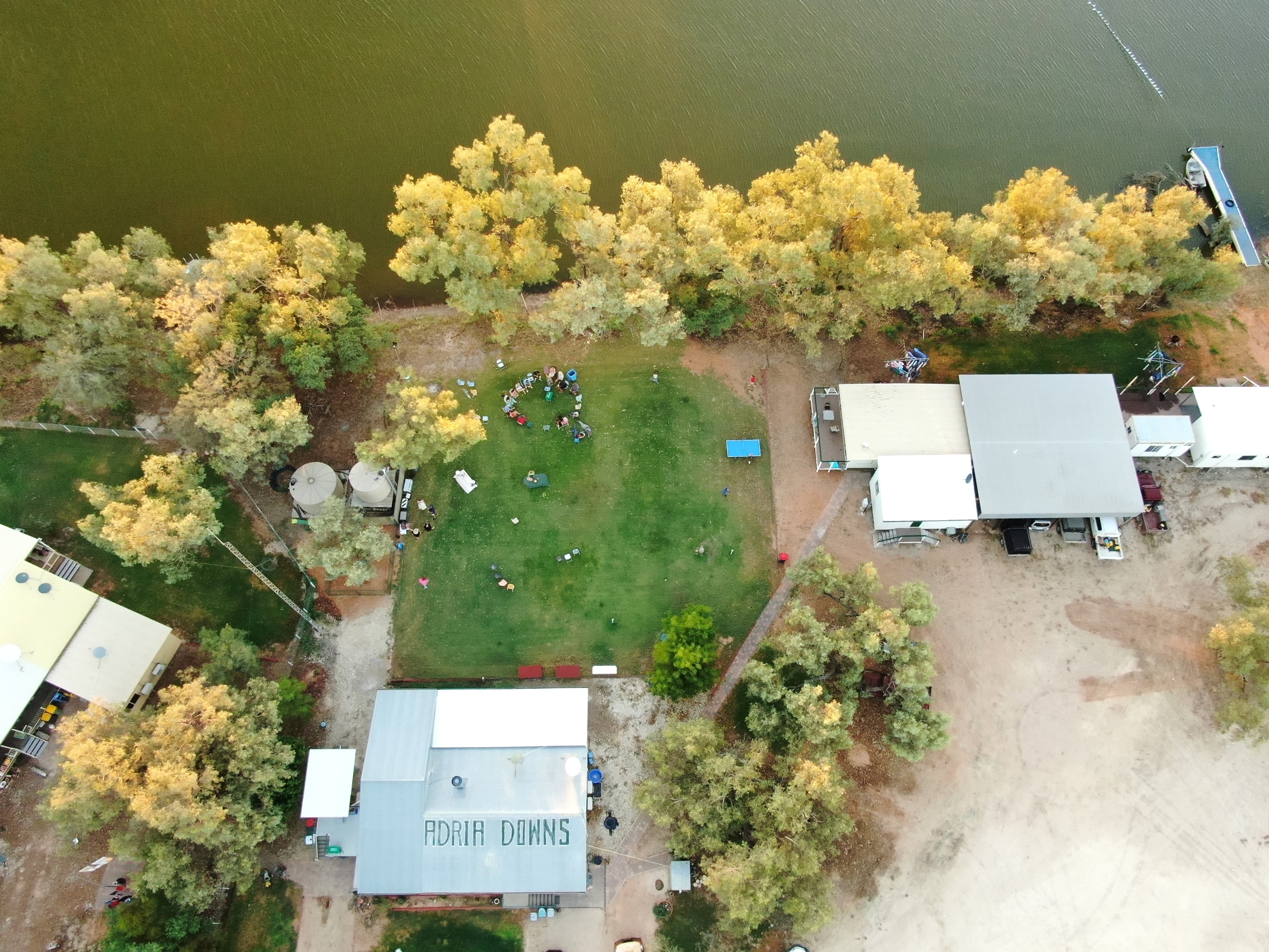 Uma vista aérea de algumas casas e um círculo de pessoas em pé em um gramado verdejante. 