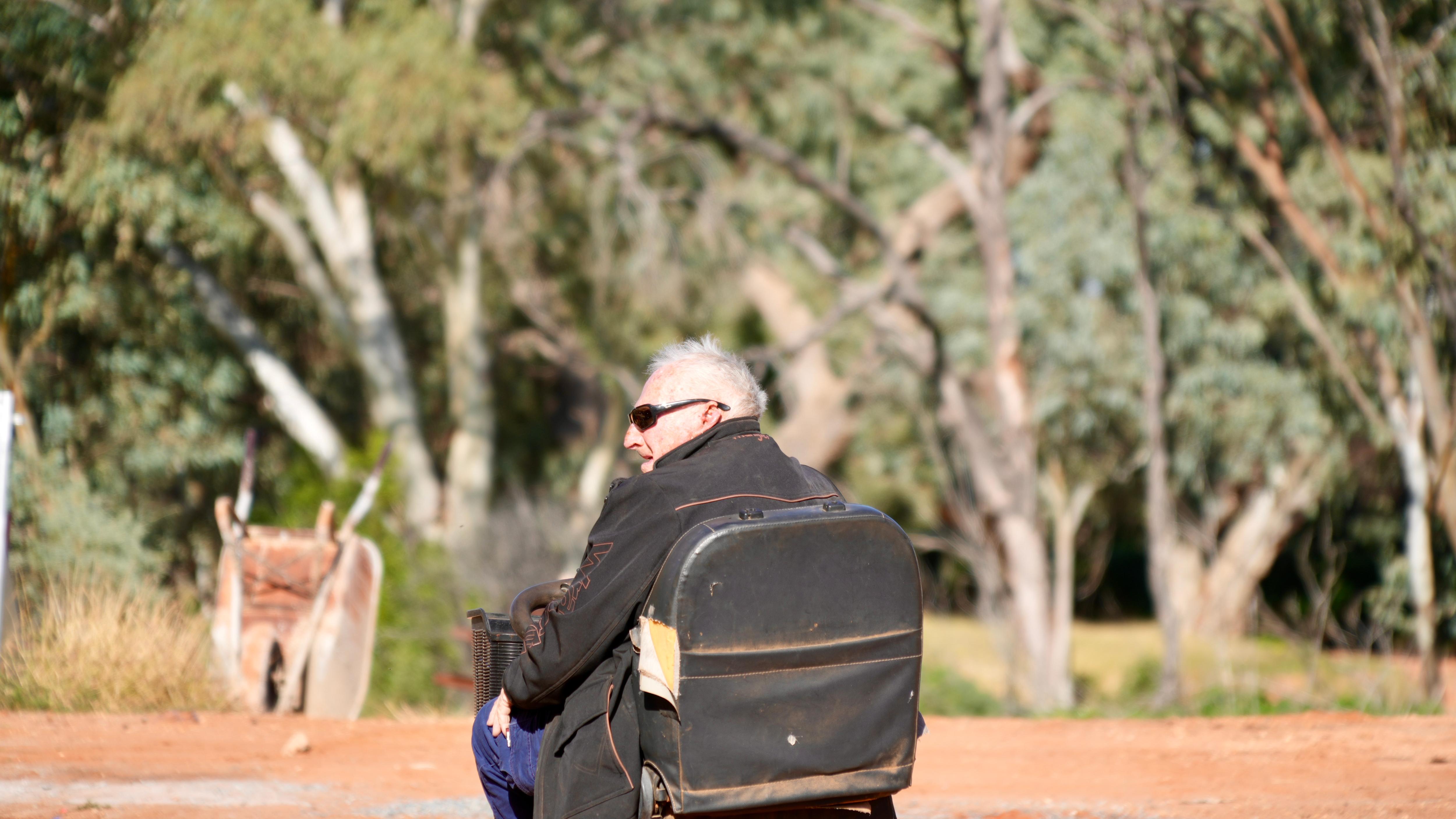 a man with grey hard and sunglasses sitting on a gopher mobile with red dirt and trees in the background