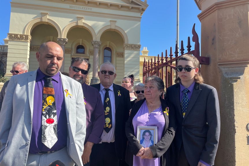 Five people stand outside court wearing purple