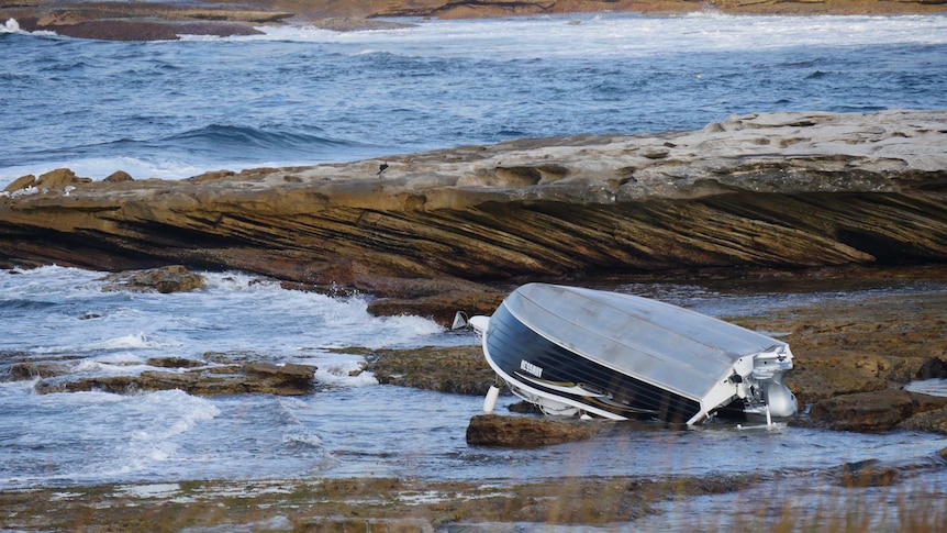 A capsized boat on rocks in Botany Bay.