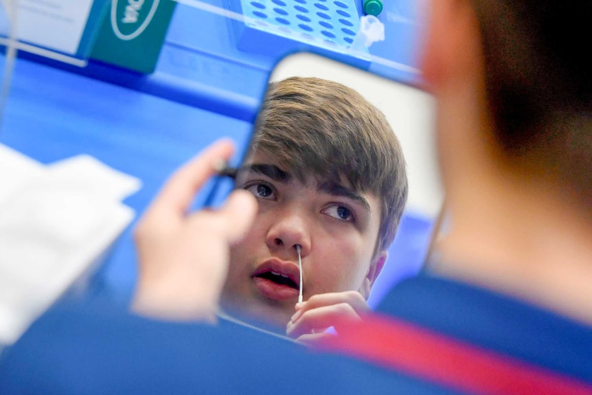 A teenaged boy holding a swab to his nose in front of a mirror