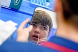 A teenaged boy holding a swab to his nose in front of a mirror