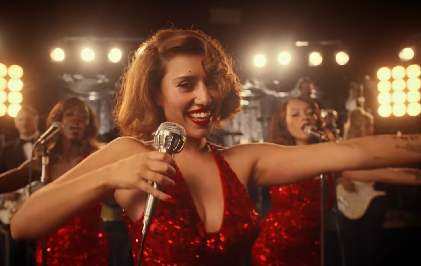 Raye se pone de pie y sonríe con un vestido rojo de lentejuelas y un micrófono antiguo en su vídeo musical.