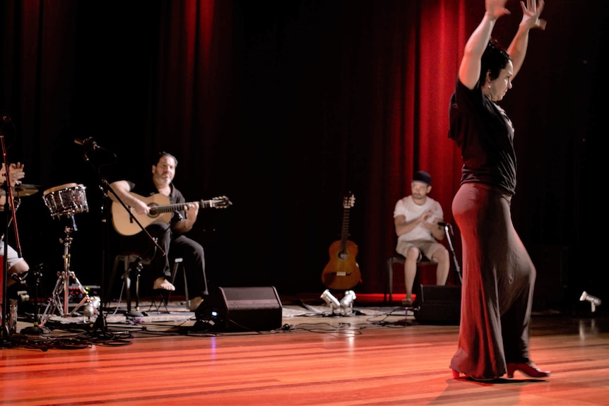 Una bailarina con las manos levantadas en el aire mientras los músicos tocan de fondo