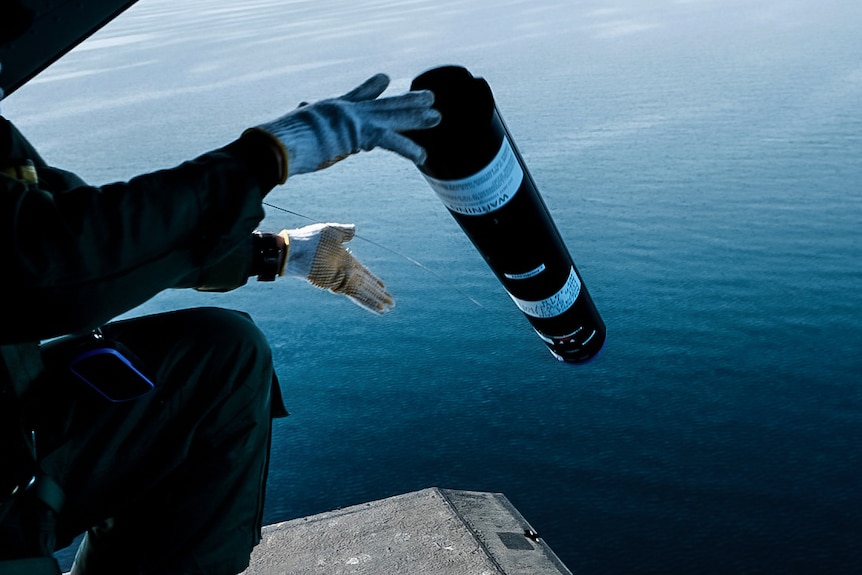 A black cylindrical probe is dropped from the back of a helicopter into the ocean.