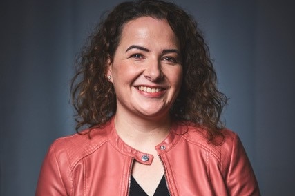 Alison stands wearing a coral-coloured leather jacket over a black top