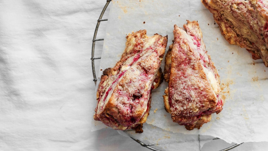 Two triangular scones cool on a baking tray with swirls of raspberry, sugar and white chocolate, to illustrate our recipe.