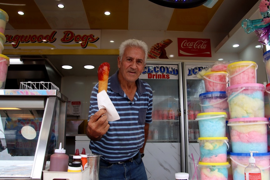   Un vendeur de nourriture tient une saucisse frite trempée dans une sauce rouge