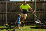 a young boy dragging a toy lawnmower next to his father who has a real lawnmower