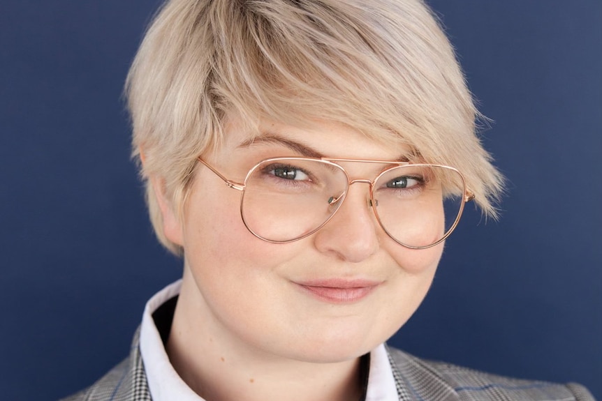 A headshot from a young actor with cropped blonde hair and wire-rimmed glasses