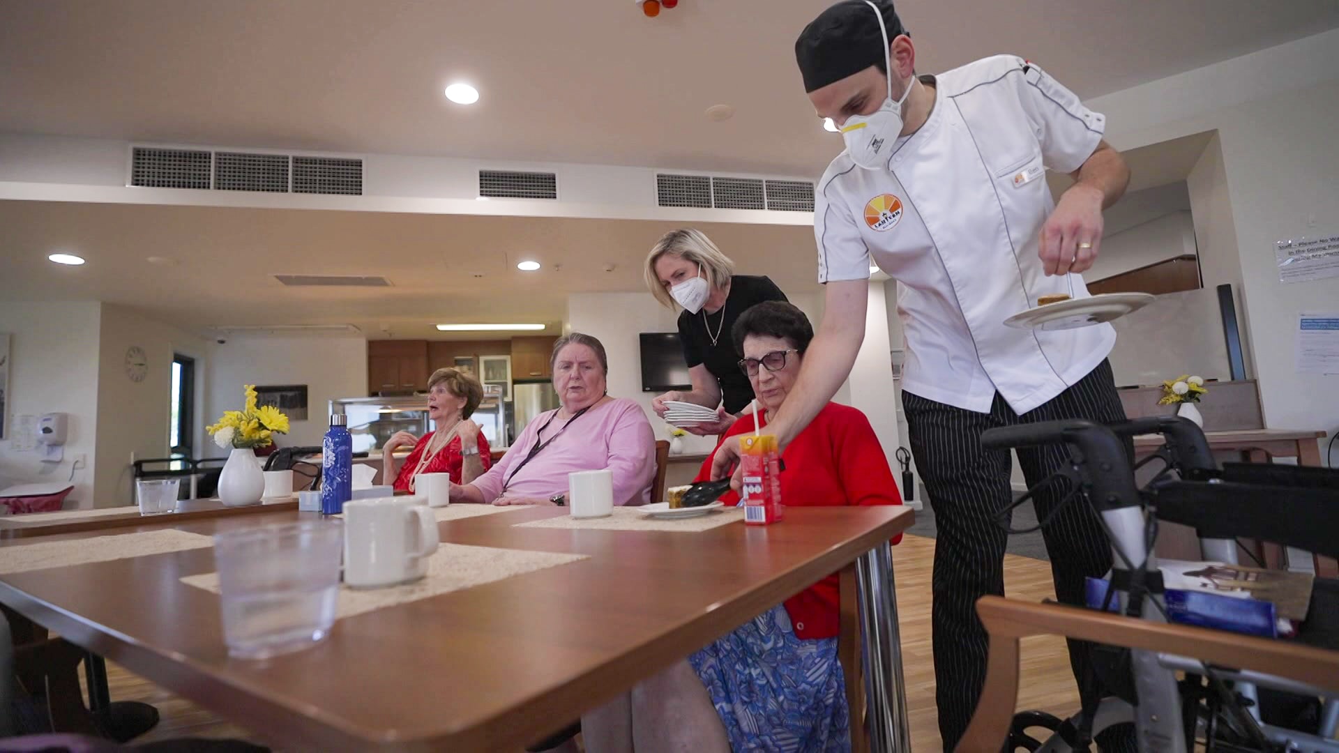 A chef and woman serve cake to aged care residents sitting at a table