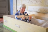 An alive elderly woman smiles as she lies in her handmade wooden coffin