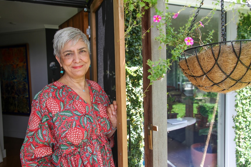 A woman stands at her door with a welcoming smile. 