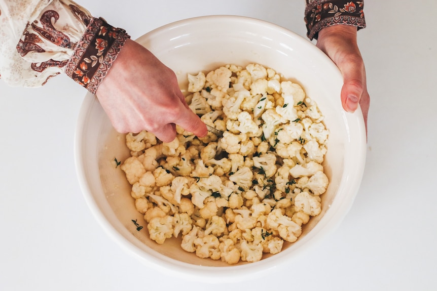 Crumbled cauliflower florets in a large mixing bowl with garlic, lemon and herbs added for flavour.