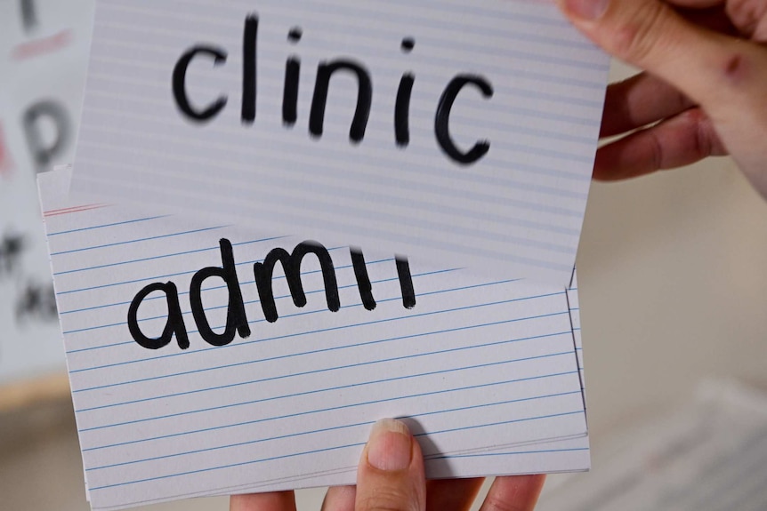 Two flash cards carrying the words 'clinic' and 'admin' are used during a reading tutorial.