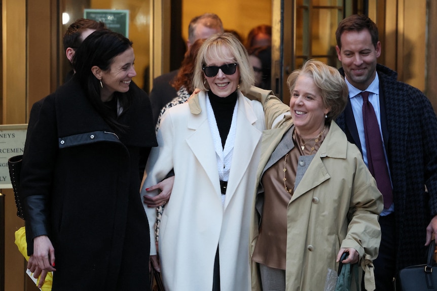 E Jean Carroll leaves the courtroom smiling in sunglasses and a white coat with lawyers 
