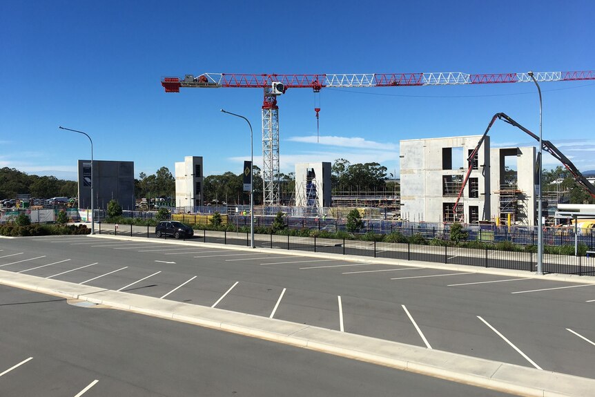 A crane on a construction site with a carpark in the foreground on a blue-sky day. 