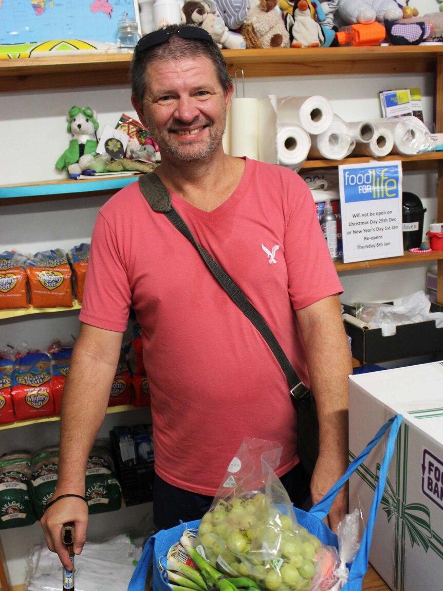 A man smiles while standing in front of a full bag of groceries.