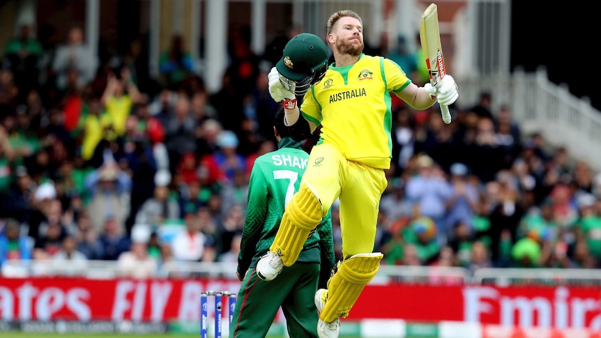 A cricketer jumps high in the air with his bat in hand as he celebrates getting 100 runs.