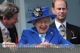 The Queen smiles from the royal balcony as she looks down on the winning horse in the main race on Derby Day.