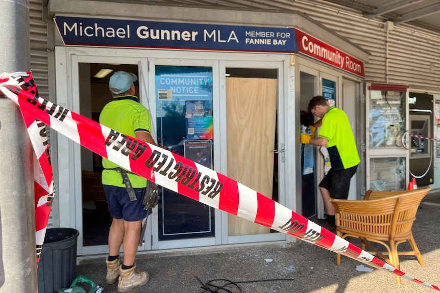 People in high-vis shirts inspect an office where glass panes are missing. Red tape is around the area.