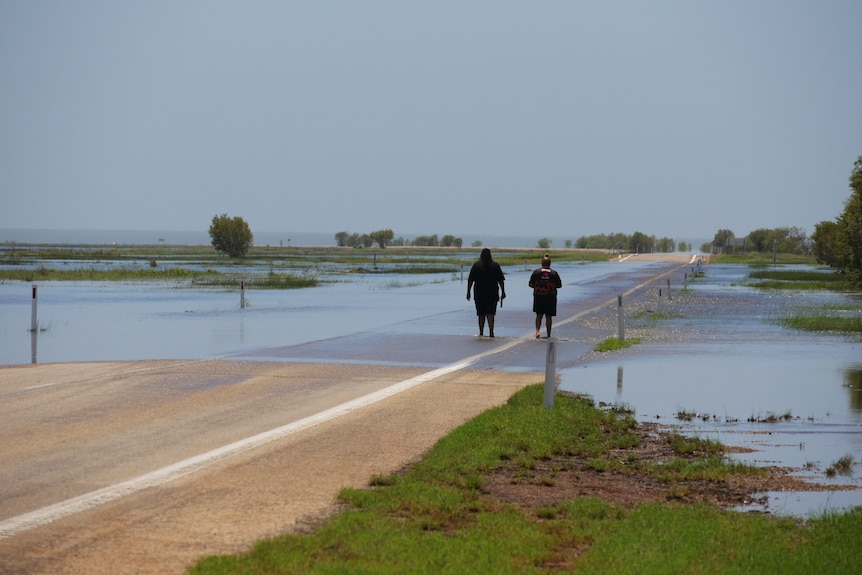 Two people standing on a partially flooded road. 