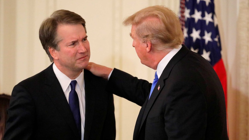 Donald Trump puts his hand on the shoulder of Brett Kavanaugh.