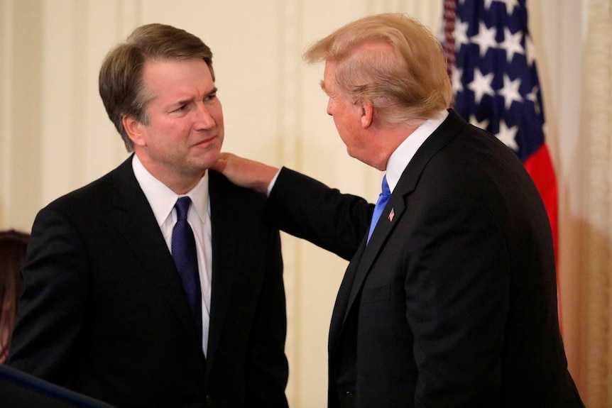 Donald Trump puts his hand on the shoulder of Brett Kavanaugh.