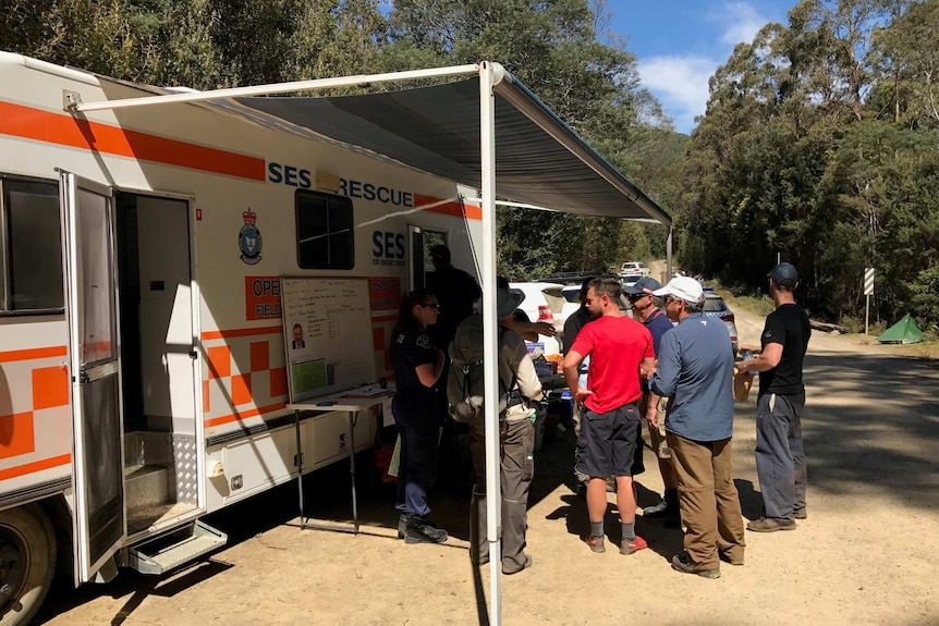 Searchers gather under police caravan awning.