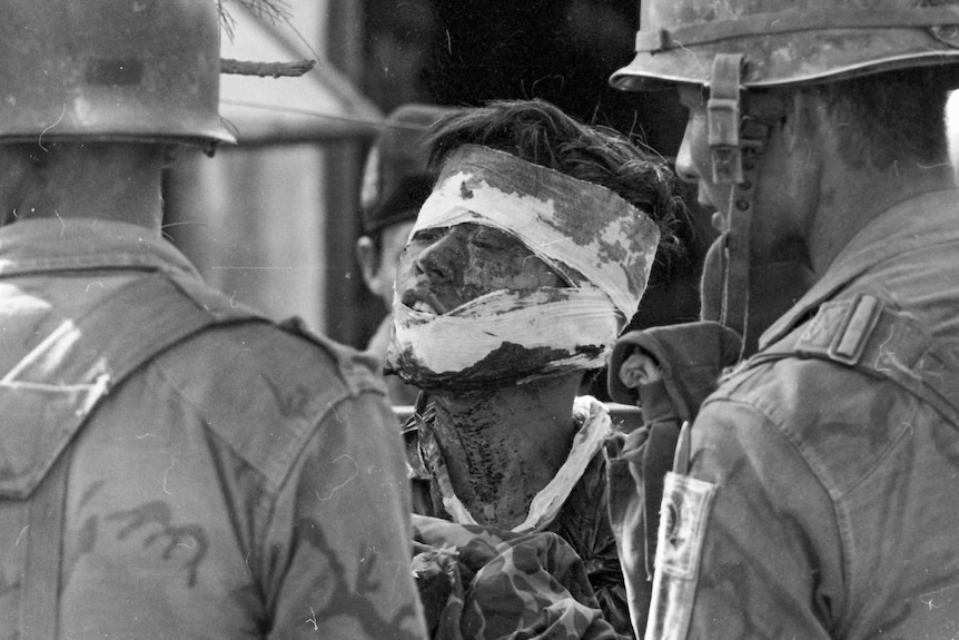 Injured North Vietnamese soldier surrounded by South Vietnamese soldiers.