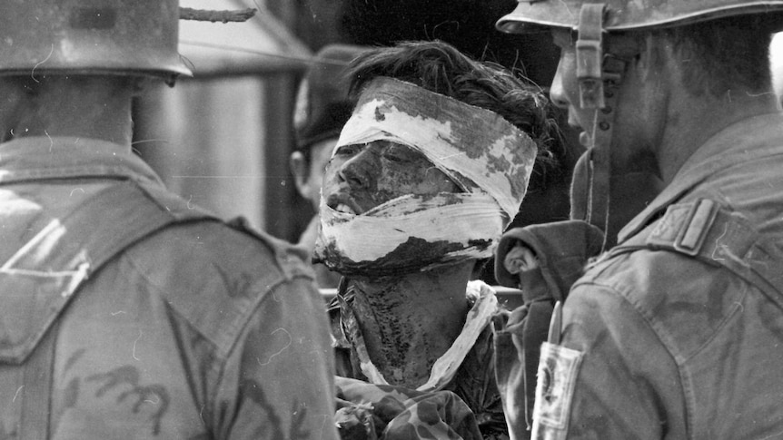 Injured North Vietnamese soldier surrounded by South Vietnamese soldiers.