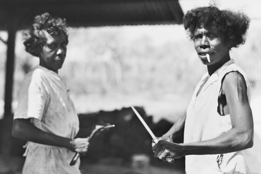 A black photo from 1942 showing two Aboriginal women holding butcher's tools, about to help prepare food at the army camp