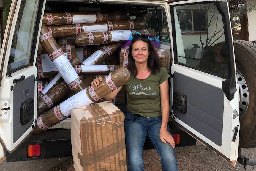 A woman sits at the back of a van with the doors open.