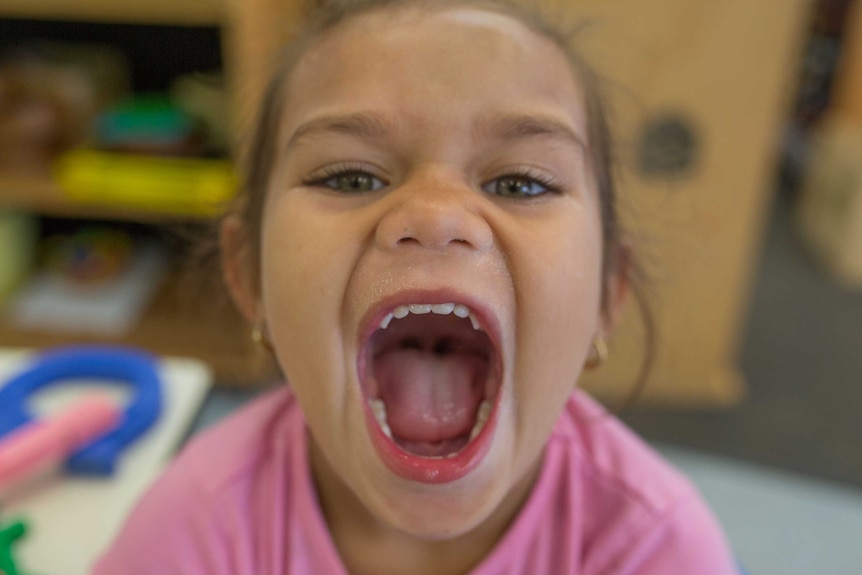 A girl opens her mouth wide as she plays up for the camera at Lulla's child care.