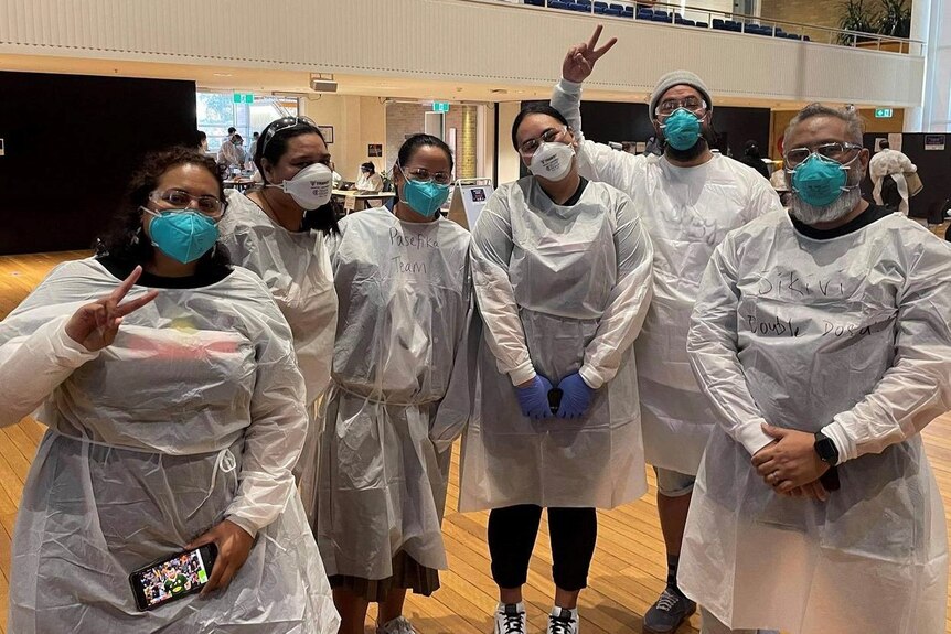 A group of Pasifika youth pose for the camera in PPE at a vaccination hub. 