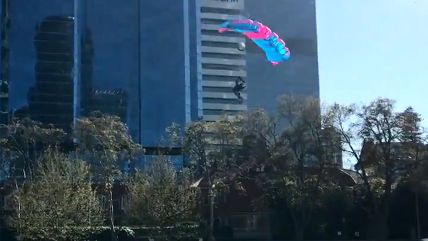 A person in a parachute in front of a tall building.