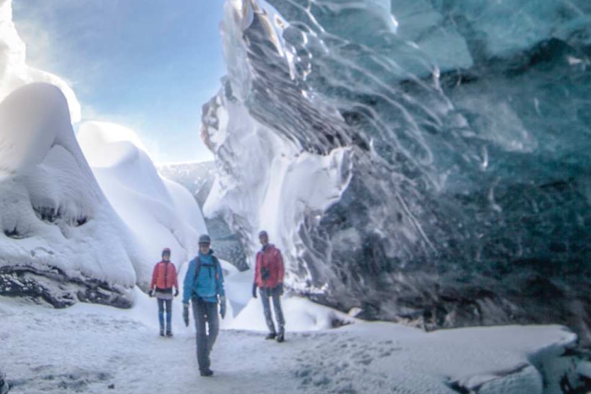 People wander inside a blue-green ice cave in Iceland